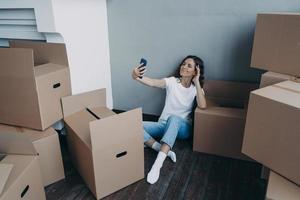 Happy woman unpacking boxes and taking selfie in new luxurious apartment. Success concept. photo