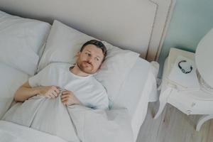 Handsome stressed young caucasian male lying in bed with his eyes open photo