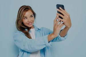 Attractive blogger taking selfie near light blue wall photo