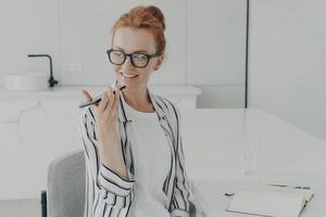 Smiling redhead woman uses virtual voice assistant records audio message photo