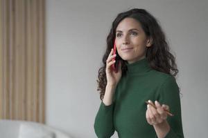 Attractive Spanish young businesswoman enjoying telephone conversation, using smartphone at work photo