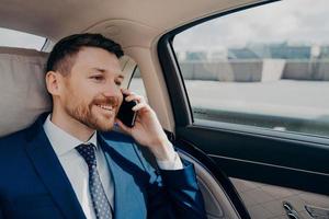 propietario de un negocio feliz sentado en el asiento trasero del coche y hablando por teléfono foto