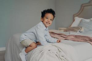 Cute young afro american boy playing on big bed at home photo