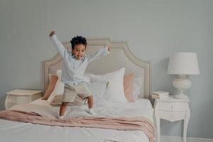 Adorable cute kid jumping cheerfully on bed and having fun at home photo