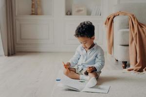 Small curly boy with colouring book at home photo