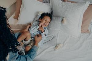 Lovely mother tickling her cute little son lying on bed and laughing photo