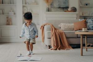 feliz niño de raza mixta disfrutando jugando solo en casa, divirtiéndose en la sala de estar foto