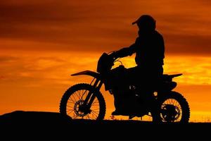 black silhouette of biker with motobike on orange sunset sky background photo