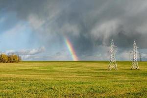 arco iris sobre el campo y postes de alta tensión foto