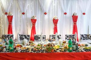 mesa de boda decorada en el salón de banquetes. mesa para recién casados decorada con cintas rojas foto