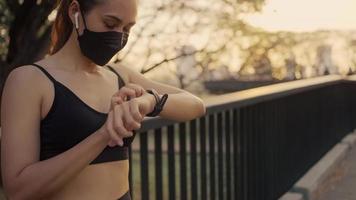 donna che indossa una maschera protettiva e imposta lo smartwatch fitness per la corsa. sportiva che controlla il dispositivo dell'orologio. video