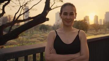 Aziatische actieve sportvrouw staat met vertrouwen na het sporten buitenshuis. portret van mooi meisje in sportkleding glimlach, en kijk naar de camera na het uitvoeren van een training voor de gezondheid in de avond in het openbare park. video