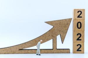 2022 New Year and Business Planning Concept. Closeup of businessman miniature figures waling with arrow sign with wooden number block on white background. photo