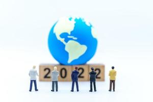 2022 New Year and Business Planning Concept. Closeup of group of businessman miniature figures standing and looking to wooden number block with mini world ball on white background. photo