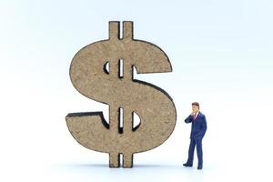 Business, Money Investment and Planning Concept. Businessman miniature figure people figure standing and looking to wooden US Dollar sign on white background. photo