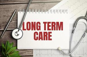 Medicine and health concept. On the table is a stethoscope, a diary and a notebook with the inscription - LONG TERM CARE photo