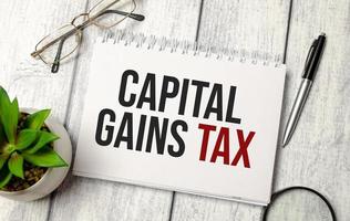capital gains tax words on notebook and pen, glasses and magnifier photo