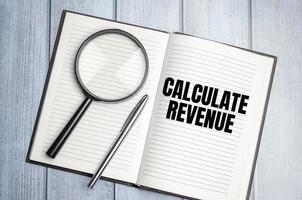 magnifying glass and a white notebook with the text CALCULATE REVENUE photo