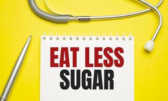 eat less sugar words on notebook and stethoscope on yellow background photo