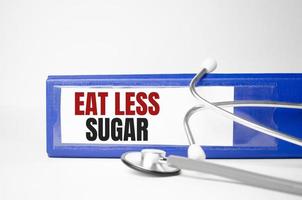 eat less sugar words on blue folder and stethoscope on wooden background photo