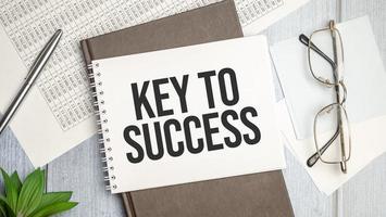 the word Key To Success, is written in a notebook lying on white table photo