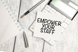 EMPOWER YOUR STAFF - text on white sticker and calculator with pen on wooden background photo