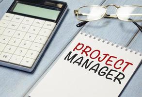 project manager word on notebook with calculator and glasses photo