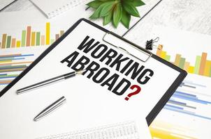 Paper with text WORKING ABROAD on the table on the chart photo