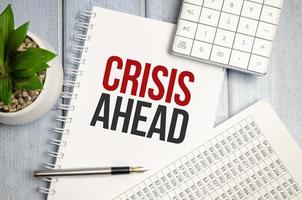 CRISIS AHEAD text on the paper sheet with paper and calculator photo