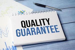 quality guarantee words on notebook and pen on wooden background photo