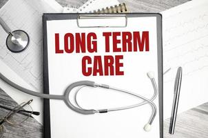 Medicine and health concept. On the table is a stethoscope, a diary and a notebook with the inscription - LONG TERM CARE photo