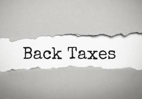 Torn white paper lies on a bright grey background with the text BACK TAXES photo
