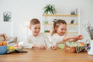 Sitting by the table. Happy little sister and brother celebrating Easter holidays together photo