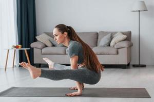 vista lateral. mujer joven con cuerpo delgado y ropa de yoga está en casa foto