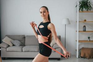 Measuring the waist by the tape. Young woman with slim body type and in yoga clothes is at home photo