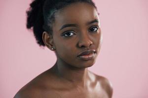 Looking in the camera. Portrait of young african american woman that is against pink background photo