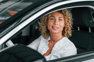 Using phone. Woman with curly blonde hair is in autosalon photo