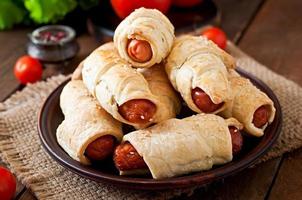 Sausage in the dough sprinkled with sesame seeds on a wooden background in rustic style photo