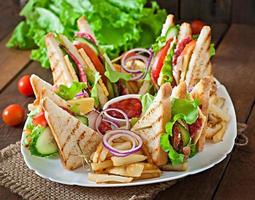 Club sandwich with cheese, cucumber, tomato, smoked meat and salami. Served with French fries. photo