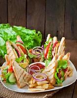 club sandwich con queso, pepino, tomate, carne ahumada y salami. servido con papas fritas. foto