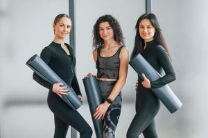 sosteniendo colchonetas de yoga. mujeres en ropa deportiva de pie en el gimnasio foto