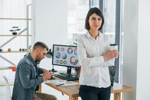 mujer de pie frente al hombre que está sentado junto a la mesa. dos diseñadores trabajando juntos en la oficina foto