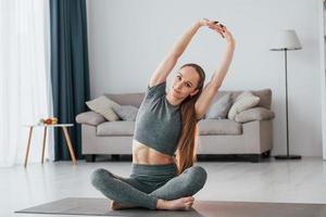 sentado en el suelo. mujer joven con cuerpo delgado y ropa de yoga está en casa foto