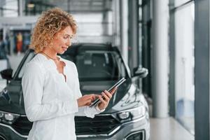 In official white shirt. Woman with curly blonde hair is in autosalon photo