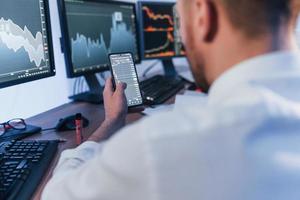 Using phone. Stock trader working in the office with exchange technology photo
