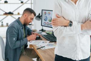 mujer de pie frente al hombre que está sentado junto a la mesa. dos diseñadores trabajando juntos en la oficina foto