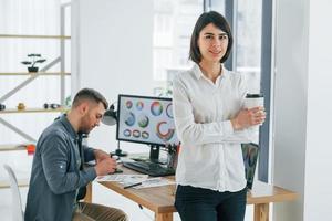 mujer de pie frente al hombre que está sentado junto a la mesa. dos diseñadores trabajando juntos en la oficina foto