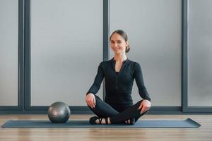 sentado en la estera de yoga. mujer con ropa deportiva está en el estudio foto