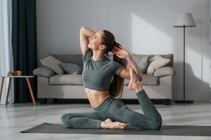 Stretching the legs. Young woman with slim body type and in yoga clothes is at home photo