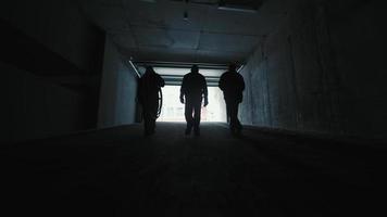 silhueta de três engenheiros de produção trabalhando na luz. funcionários de uma construtora saindo do estacionamento subterrâneo na rua. video